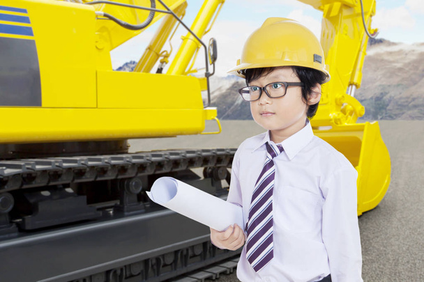 Little kid with safety helmet and blueprint pose in front of tractor on a con - Foto, Bild