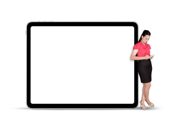 Businesswoman holding a digital tablet leaning on empty billboard - Foto, Bild