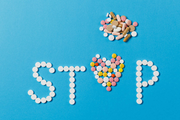 Medication white, colorful round tablets in word Stop isolated on blue background. Pills heart shape, form, letter. Concept of health, treatment, choice, healthy lifestyle. Copy space advertisement. - Photo, image