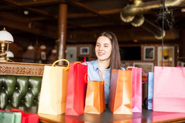 Gorgeous brunette woman sitting in a bistro with a lot of colored gift bags - 写真・画像