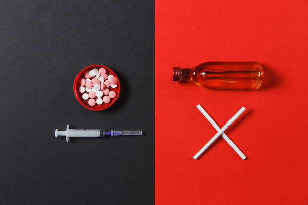 Medication round tablets pills, empty syringe needle, bottle with alcohol cognac, whiskey, two crossed cigarettes on black red background. Choice healthy lifestyle. Copy space for advertising. - 写真・画像