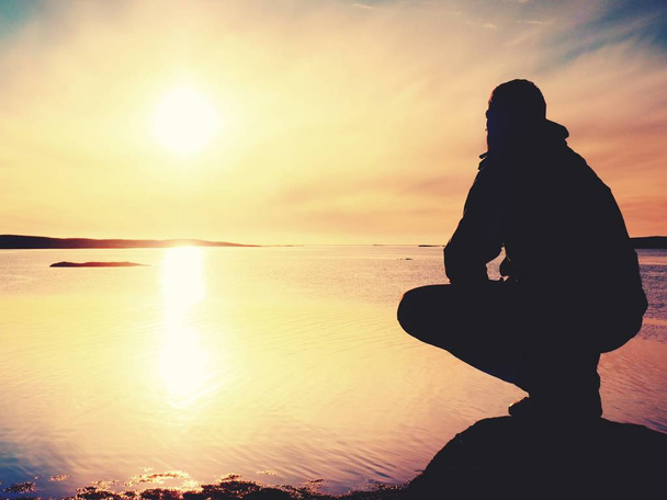 El caminante solitario se sienta solo en la costa y disfruta de la puesta de sol. Vista sobre acantilado rocoso al océano
 - Foto, Imagen