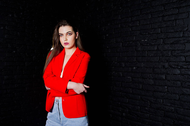 Stylish brunette girl on red jacket against studio black brick w - Фото, зображення
