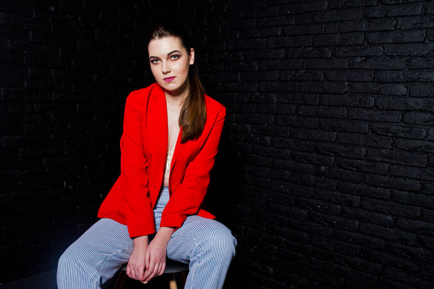 Stylish brunette girl on red jacket against studio black brick w - Foto, imagen