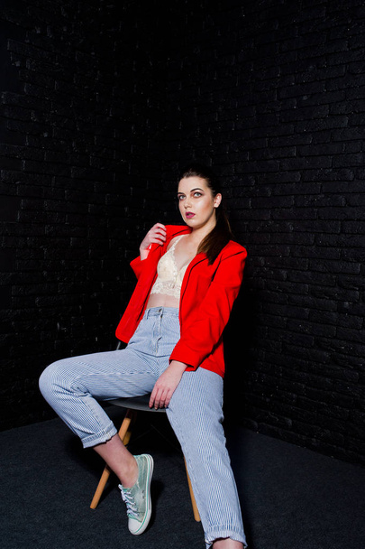 Stylish brunette girl on red jacket against studio black brick w - Valokuva, kuva