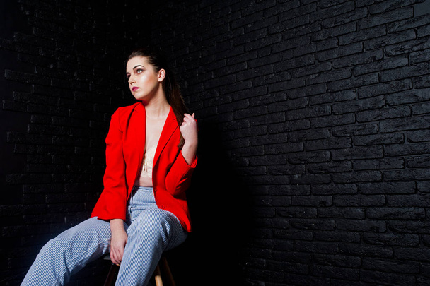 Stylish brunette girl on red jacket against studio black brick w - Φωτογραφία, εικόνα