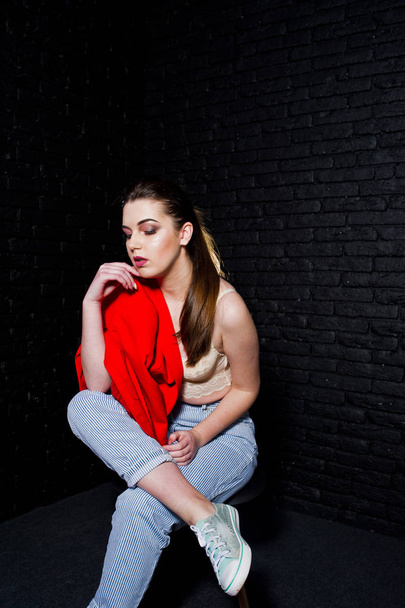 Stylish brunette girl on red jacket against studio black brick w - Fotografie, Obrázek
