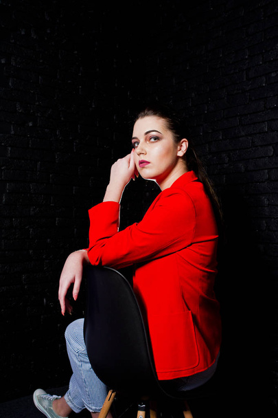 Stylish brunette girl on red jacket against studio black brick w - Zdjęcie, obraz