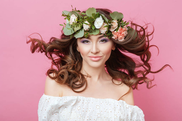 Portret van mooie seksuele sensuele jongedame met perfecte huid make-up streaming haren en bloemen op hoofd op roze achtergrond. Krans van bloemen Spring Summer Fashion Lifestyle mensen concepten. - Foto, afbeelding
