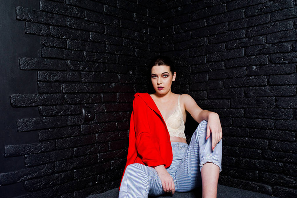 Stylish brunette girl on red jacket against studio black brick w - Foto, afbeelding