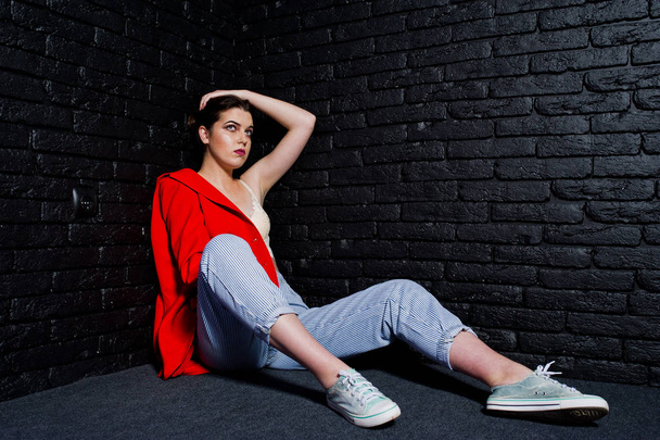 Stylish brunette girl on red jacket against studio black brick w - Foto, afbeelding