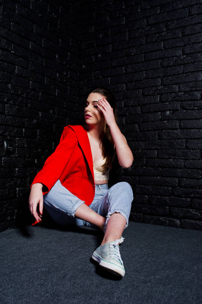 Stylish brunette girl on red jacket against studio black brick w - Фото, зображення