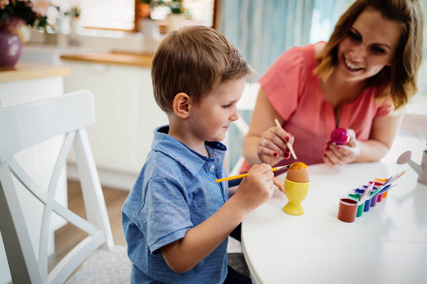 Young mother and her cute son having fun while painting eggs for Easter - Foto, imagen