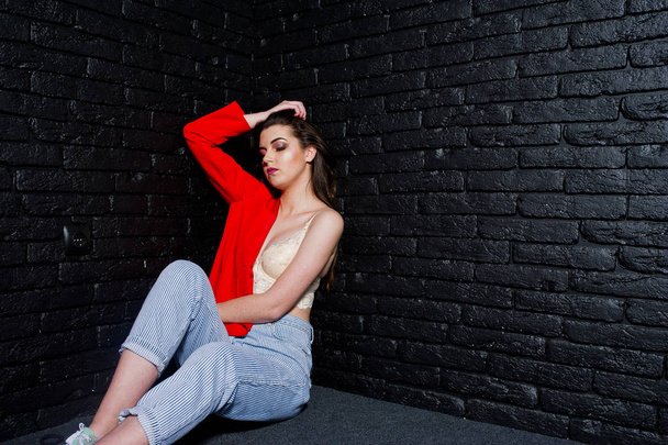Stylish brunette girl on red jacket against studio black brick w - Valokuva, kuva