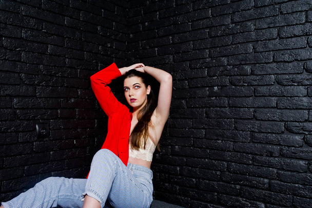 Stylish brunette girl on red jacket against studio black brick w - Фото, изображение