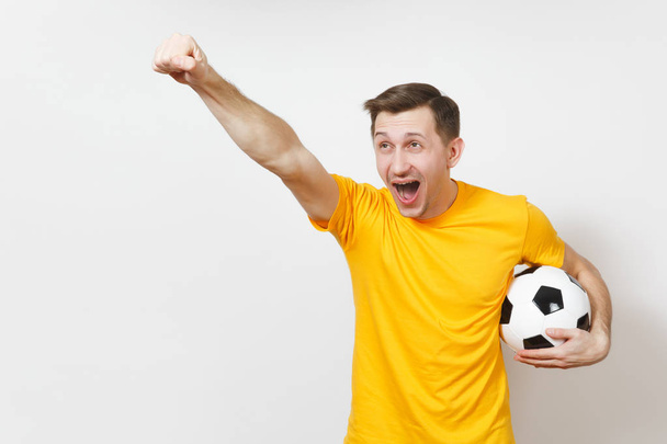 Ευρωπαϊκή εμπνευσμένη νεαρός, ανεμιστήρα ή παίκτη σε κίτρινο ομοιόμορφη κρατήσει μπάλα ποδοσφαίρου, ευθυμία αγαπημένη ποδοσφαιρική ομάδα, εκφραστική χειρονομώ χέρια που απομονώνονται σε λευκό φόντο. Έννοια τρόπου ζωής. Χώρο αντίγραφο. - Φωτογραφία, εικόνα