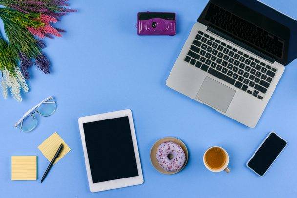 vista superior de dispositivos digitales, flores, taza de café con donut y cámara en azul
   - Foto, Imagen