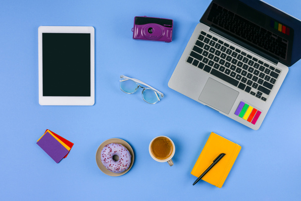 вид сверху ноутбука, цифровой планшет, чашка кофе с пончиком и камера на голубом
  - Фото, изображение