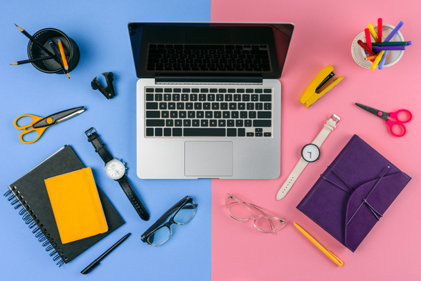 Draufsicht auf Laptop mit leerem Bildschirm, Brille, Armbanduhr und Notizbuch aufgeteilt am männlichen und weiblichen Arbeitsplatz - Foto, Bild