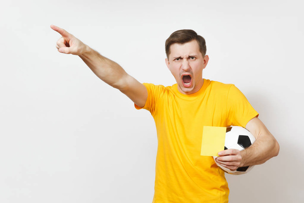 深刻な深刻な欧州青年、サッカーの審判または黄色い制服黄色のカードを示す、白い背景で隔離のサッカー ボールを保持しているプレーヤー。スポーツ、サッカー、健康的なライフ スタイルのコンセプト. - 写真・画像