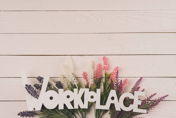 top view of beautiful blooming flowers and word workplace on wooden surface - Foto, imagen