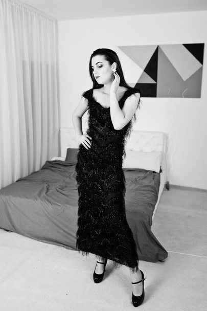 Brunette girl in black evening dress against white room with bed - Foto, imagen