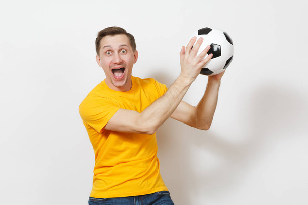 Geïnspireerd vrolijke Europese jongeman, ventilator of speler in geel uniform greep vangst voetbal, cheer favoriete voetbalteam geïsoleerd op een witte achtergrond. Sport voetballen, gezonde levensstijl concept. - Foto, afbeelding