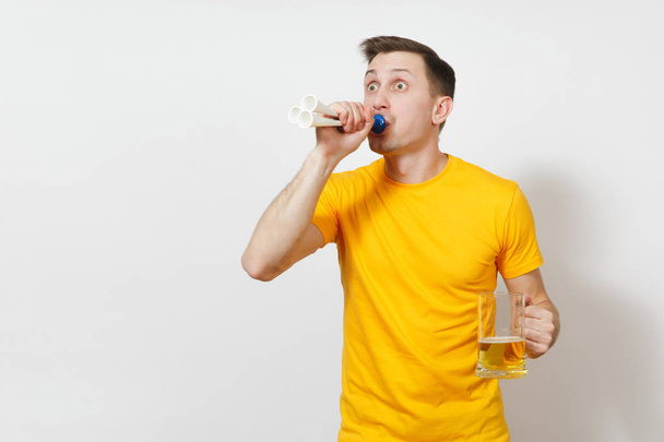 Inspired young fun cheerful European man, fan or player in yellow t-shirt hold pint mug of beer, football pipe cheer favorite team isolated on white background. Sport, student, play lifestyle concept. - Photo, Image