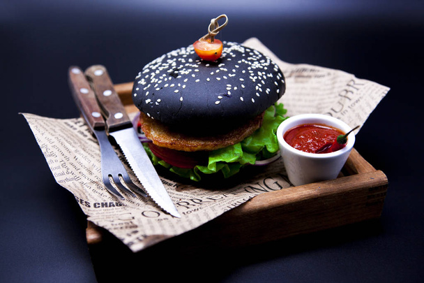 Juicy black fish burger. Burger with a knife fork and chili sauce on the newspaper - Фото, зображення