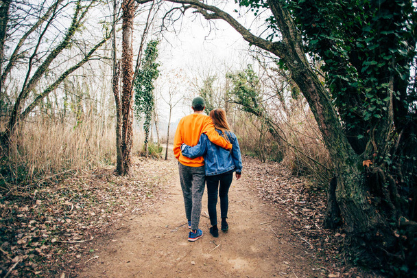 Cute and adorable couple of two hipsters, boy and girl, skip school for walk in park or forest on hike trail or path, explore together during trip. Hug in affectionate manner, wear fashionable outfits - Фото, изображение