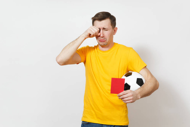 European sad upset crying shocked young man, football fan or player in yellow uniform hold in hand red soccer card for retire from field isolated on white background. Sport play, lifestyle concept. - Fotó, kép