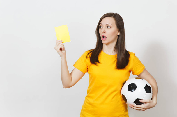 Evropské vážné těžké mladá žena, fotbalový rozhodčí nebo přehrávač v žlutých uniformách ukazuje žlutou kartu, drží fotbalový míč izolovaných na bílém pozadí. Sport hraje fotbal, koncept zdravého životního stylu. - Fotografie, Obrázek