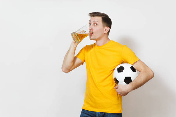 Inspired young fun cheerful European man, fan or player in yellow uniform drink pint mug of beer, soccer ball cheer favorite football team isolated on white background. Sport, play, lifestyle concept. - Photo, Image