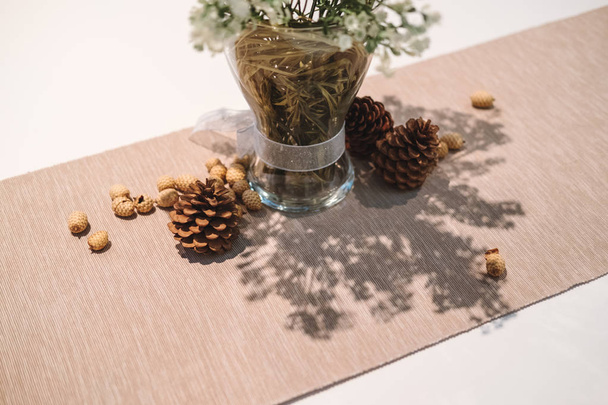 Table decorations, pine cones with glass vase and flowers on dining table - Photo, Image