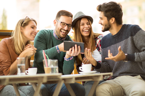 Grupo de cuatro amigos tomando un café juntos, hablando y disfrutando de su tiempo usando tableta digital
. - Foto, imagen