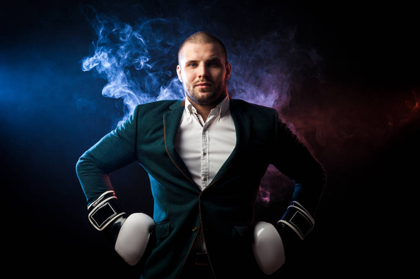 Beau sportif homme en chemise blanche, veste verte, gants de boxe noir et blanc posant contre la fumée rouge et bleue d'une lingette sur un fond noir isolé
 - Photo, image