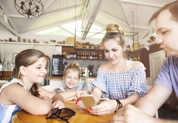  Happy family with two daughters having dinner and using smartph - Фото, зображення