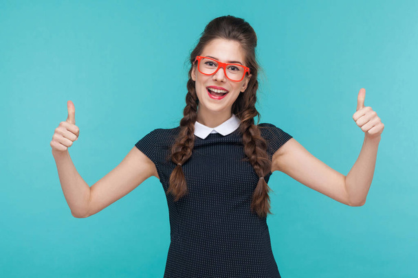 successful woman in dress and red glasses showing thumbs up at camera on blue background - Zdjęcie, obraz