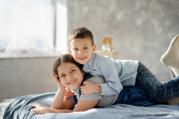 Two children, the boy and the girl, lie on a bed. The younger brother embraces elder sister for shoulders. Children have a good mood. - Фото, зображення