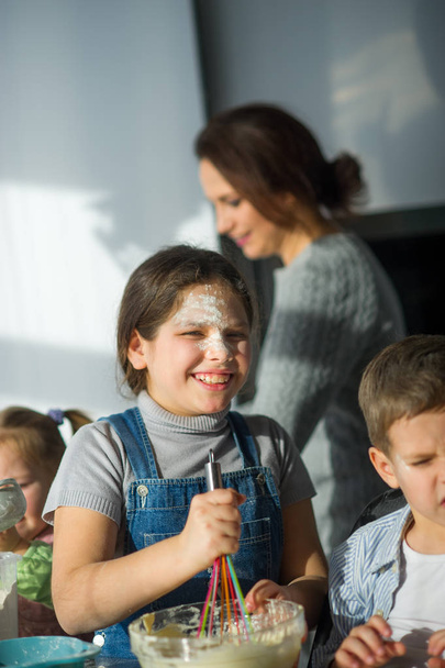 Matka i trójka dzieci przygotowują coś z ciasta. Dzieci bardzo to lubią. Ich twarze w mące, ciasto przykleiło się do rąk. - Zdjęcie, obraz