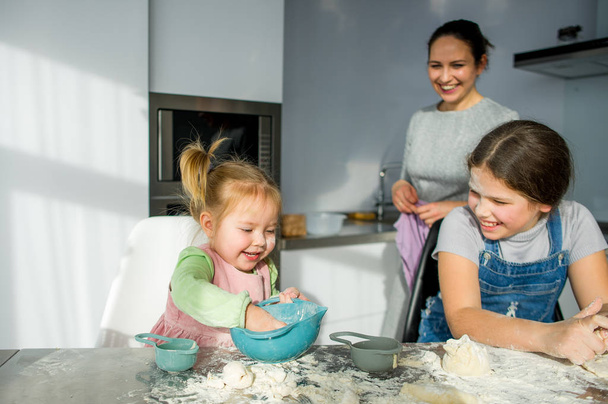 Maman apprend à deux petites filles à cuisiner avec de la pâte. Les enfants avec plaisir sont engagés dans le travail de cuisine
. - Photo, image