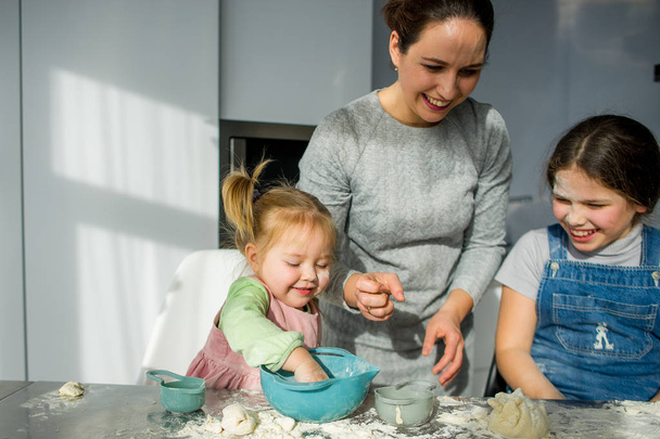 Maman apprend à deux petites filles à cuisiner avec de la pâte. Les enfants avec plaisir sont engagés dans le travail de cuisine
. - Photo, image