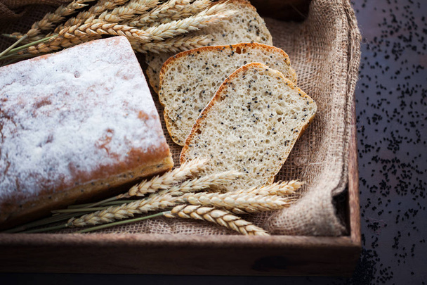 pan casero con semillas de nigella sativa, vista superior en caja con arpillera y espigas de trigo
 - Foto, Imagen