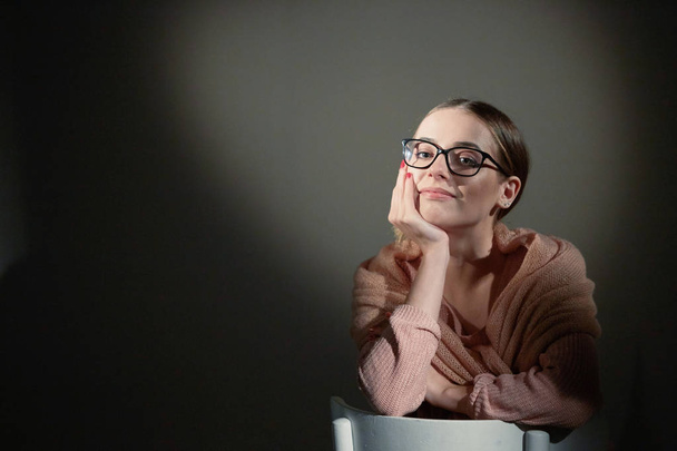 κορίτσι με τα γυαλιά στο studio σε σκούρο φόντο. κηλίδες φωτός. - Φωτογραφία, εικόνα