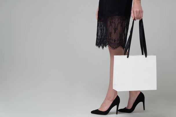 Legs of girl in black dress with white paper bag - Φωτογραφία, εικόνα