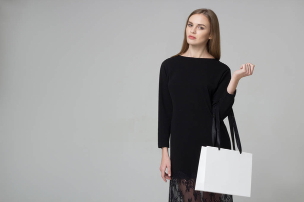 Красивая длинноволосая девушка в черном платье с белым бумажным пакетом
 - Фото, изображение