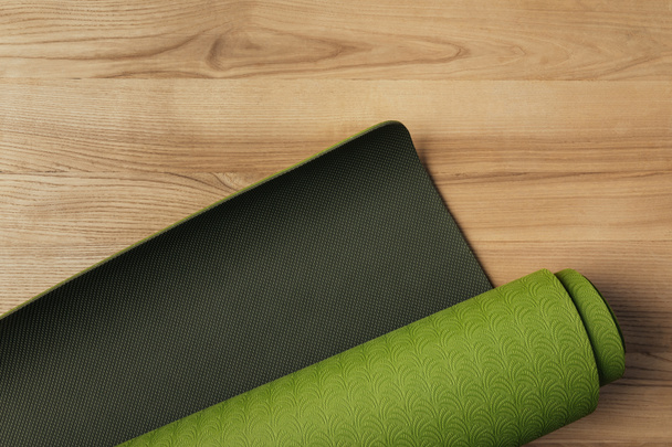 top view of green rolled yoga mat on wooden floor - Foto, Imagem