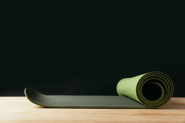 green rolled yoga mat on wooden table on black - Φωτογραφία, εικόνα