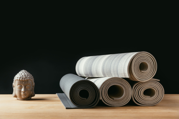 verschiedene gerollte Yogamatten und Buddha-Skulpturen auf Holztisch - Foto, Bild