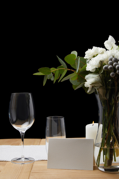 Fleurs tendres dans un vase avec des verres sur la table à côté de la carte blanche sur fond noir
 - Photo, image